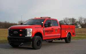 Red Swatara fire-rescue utility truck parked on a road, featuring emergency lights on top. The truck is labeled "Utility 91" with fire department insignia, set against a rural backdrop with bare trees and a farmhouse.