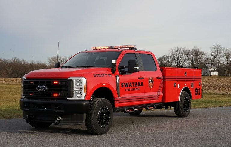 Red Swatara fire-rescue utility truck parked on a road, featuring emergency lights on top. The truck is labeled "Utility 91" with fire department insignia, set against a rural backdrop with bare trees and a farmhouse.