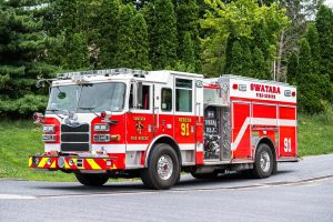 A brightly colored red and white fire truck from Swatara Fire-Rescue, marked with the number 91, is parked on a street. Green trees and grass are visible in the background.